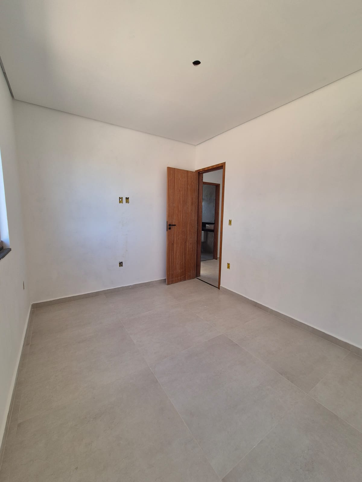 Quarto amplo com porta de madeira e piso porcelanato claro