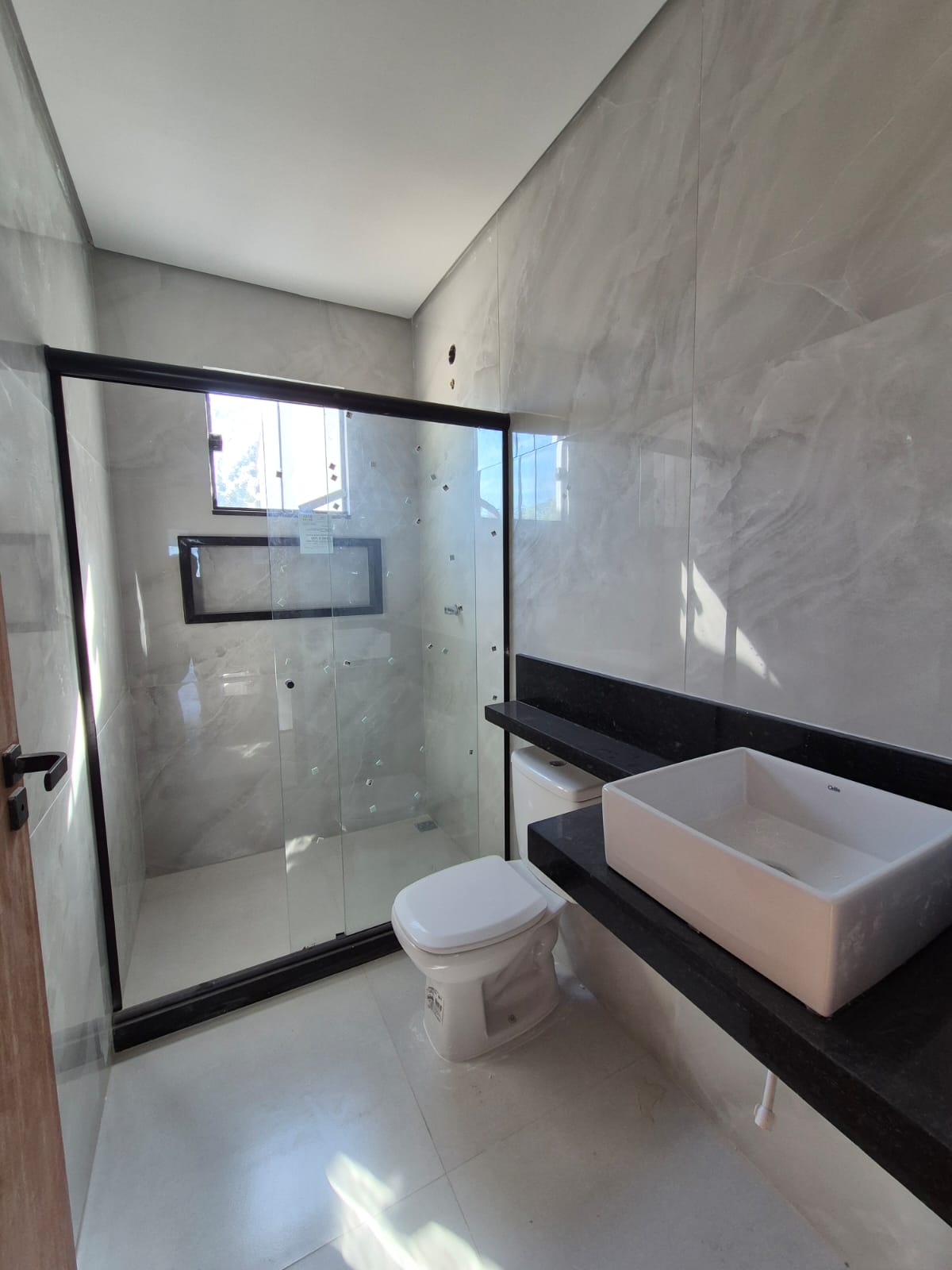 Banheiro com porcelanato marmorizado, box de vidro e bancada em granito preto