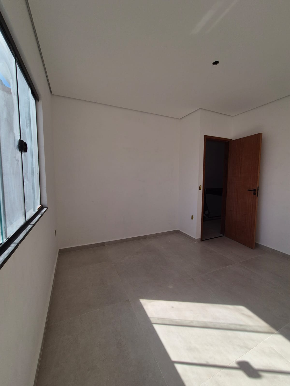 Quarto com janela ampla e luz natural sobre o piso porcelanato