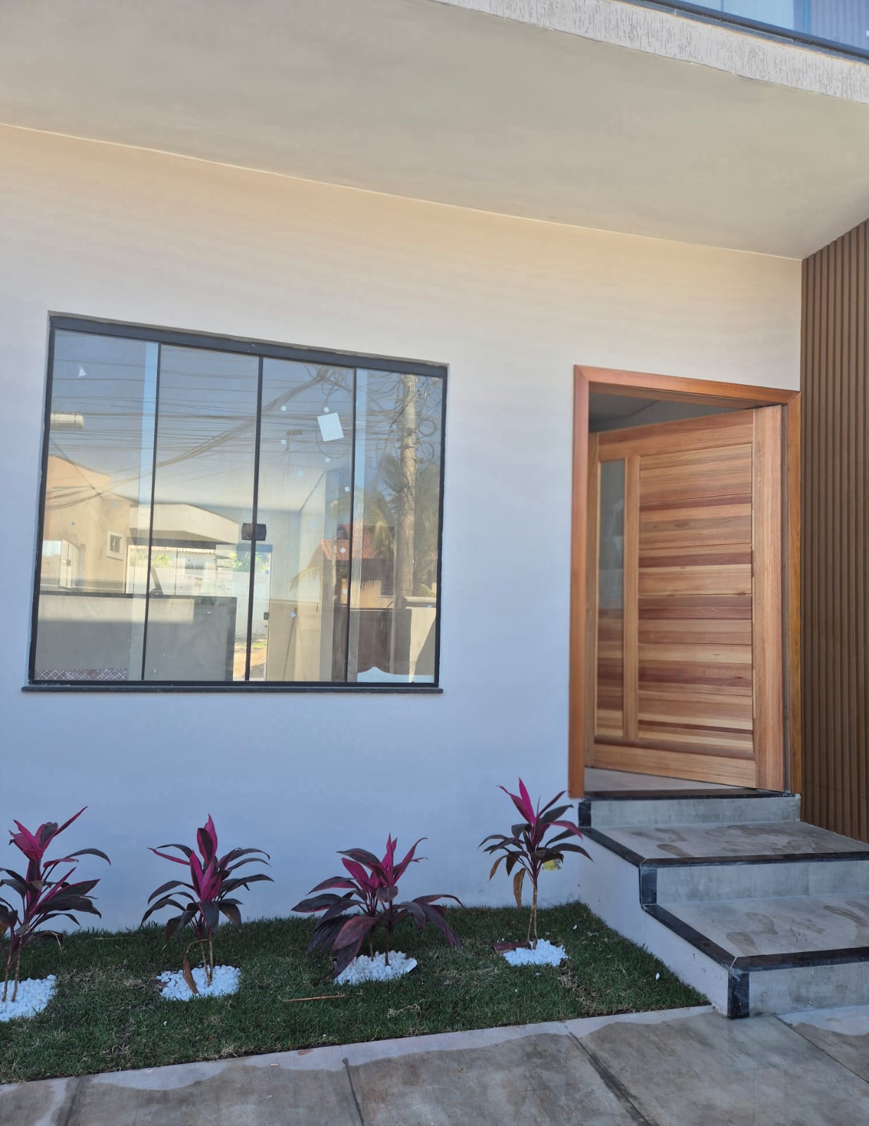 Entrada com porta pivotante de madeira e jardim de folhagens