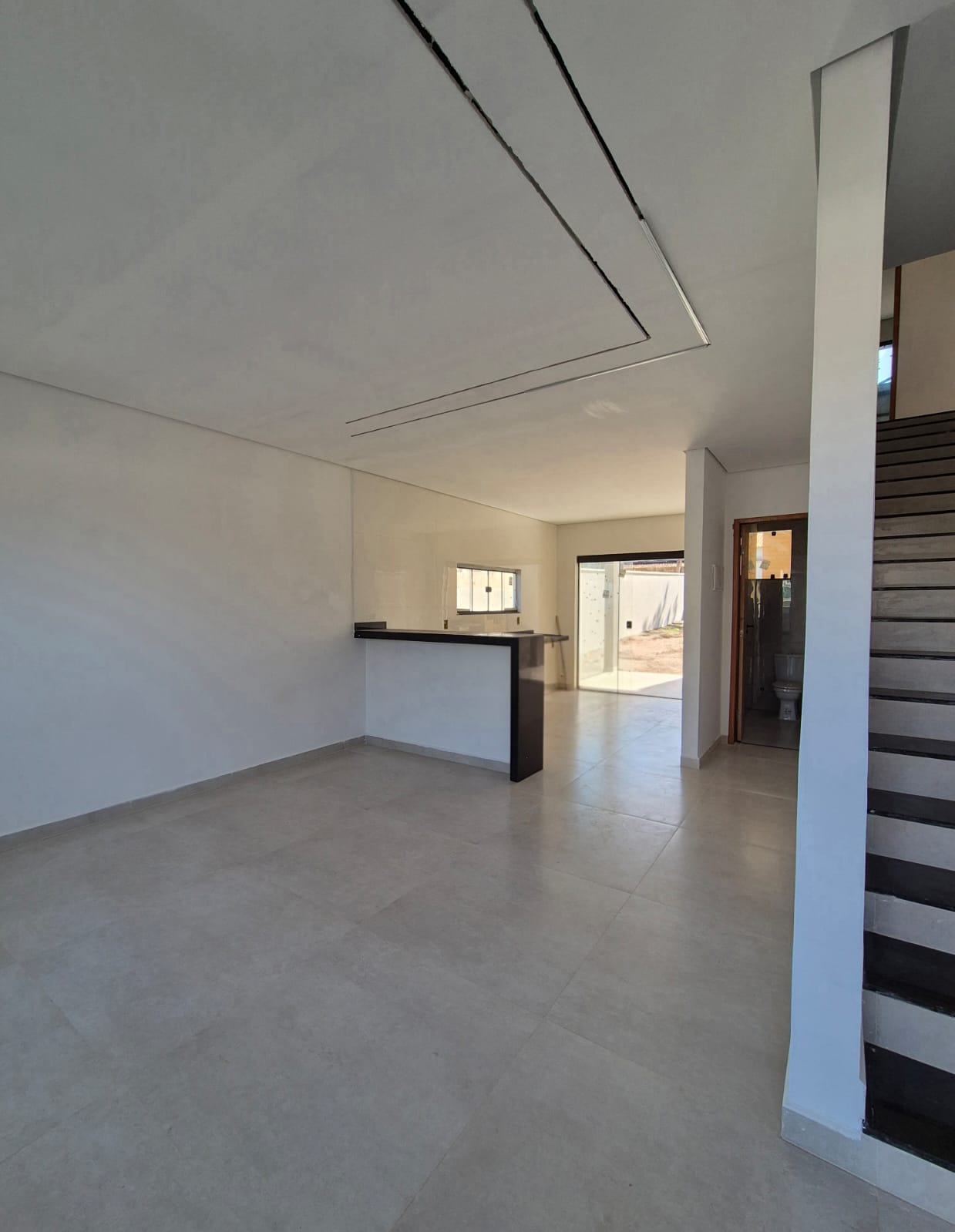 Sala integrada com sanca de gesso, piso porcelanato e bancada da cozinha ao fundo