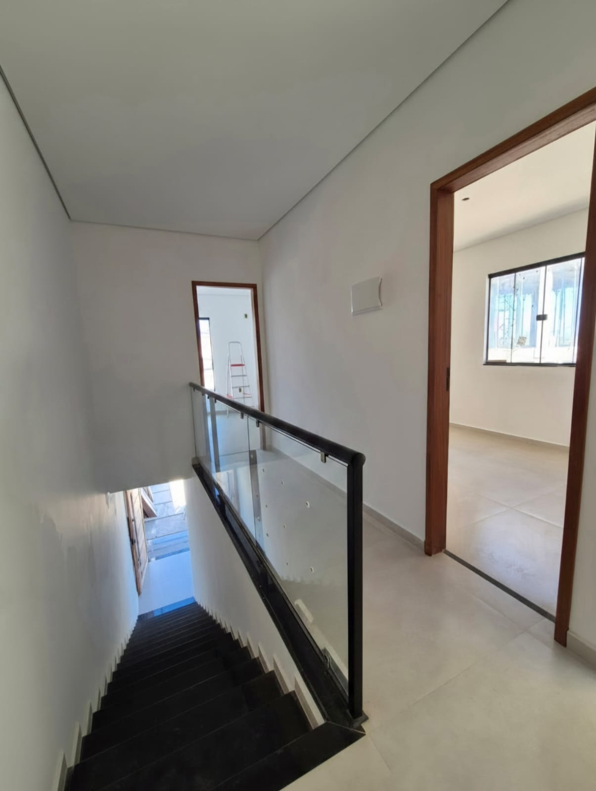 Escada em granito com guarda-corpo de vidro e circulação do pavimento superior